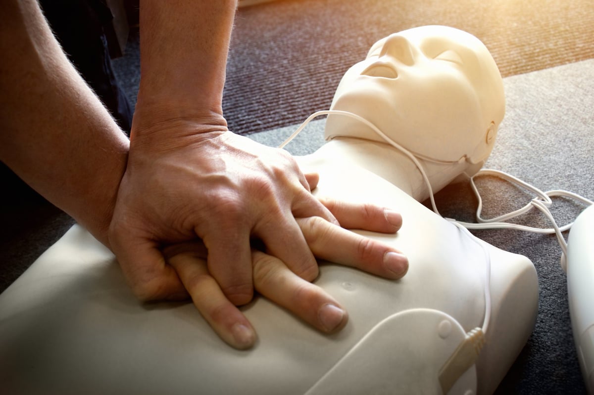 CPR AED first aid training demonstration - Cardiopulmonary emergency resuscitation medical procedure on dummy. Paramedic teaching chest compression technique to students learning about cardiac arrest via mannequin doll.